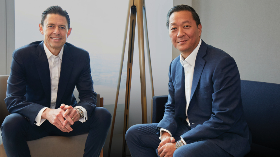 Scott Nuttall and Joe Bae sitting down together smiling at the camera. 